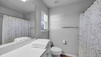 A bathroom with a white vanity, a toilet, a shower curtain, and a window with blinds.