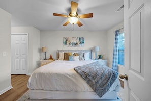 A bedroom with a bed, a ceiling fan, a nightstand, a lamp, a window with curtains, and a door. - 3-bedroom house in adorable Raleigh with cool AC, charm and pool access (Raleigh)