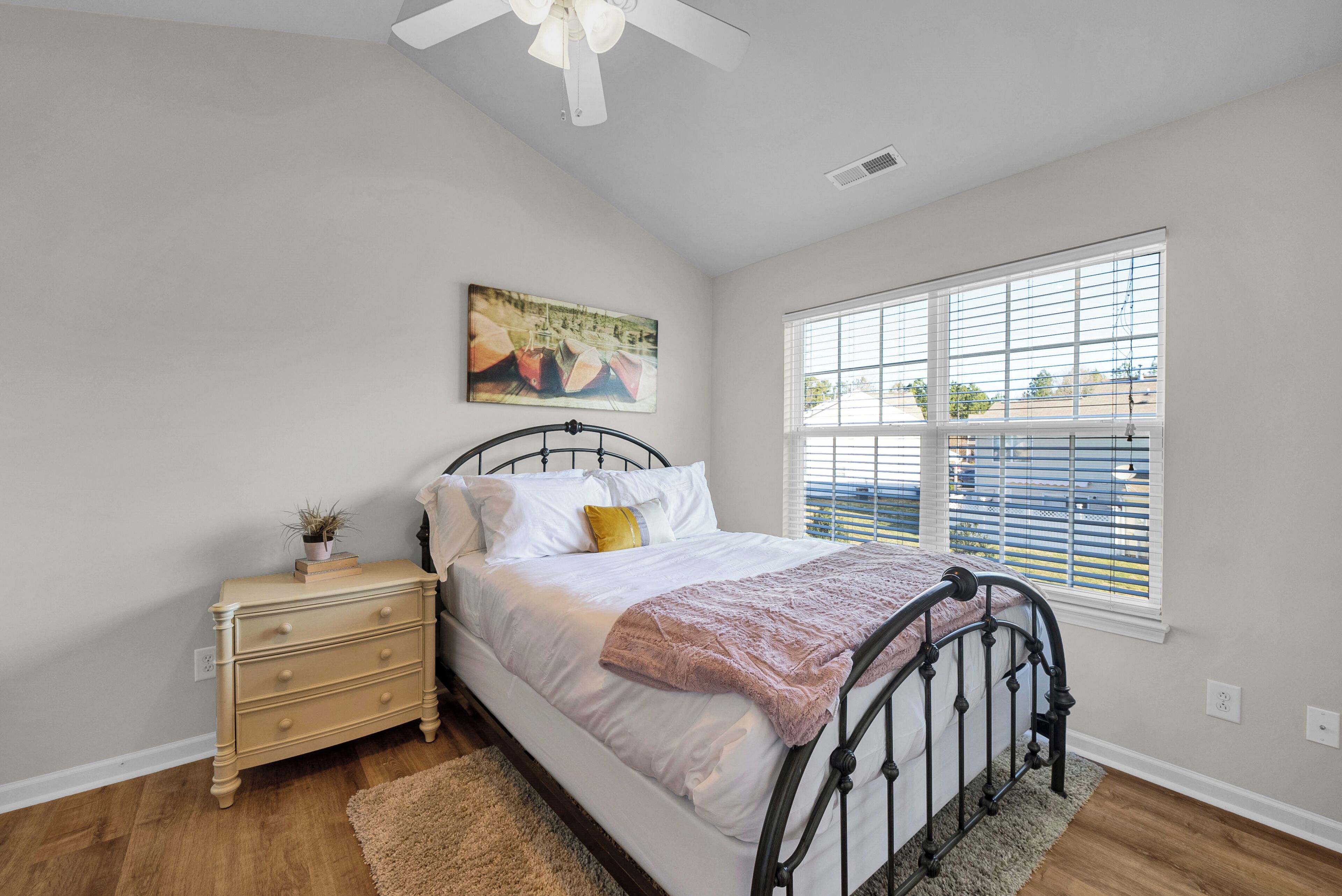 A bedroom with a bed, a nightstand, a window, and a ceiling fan.