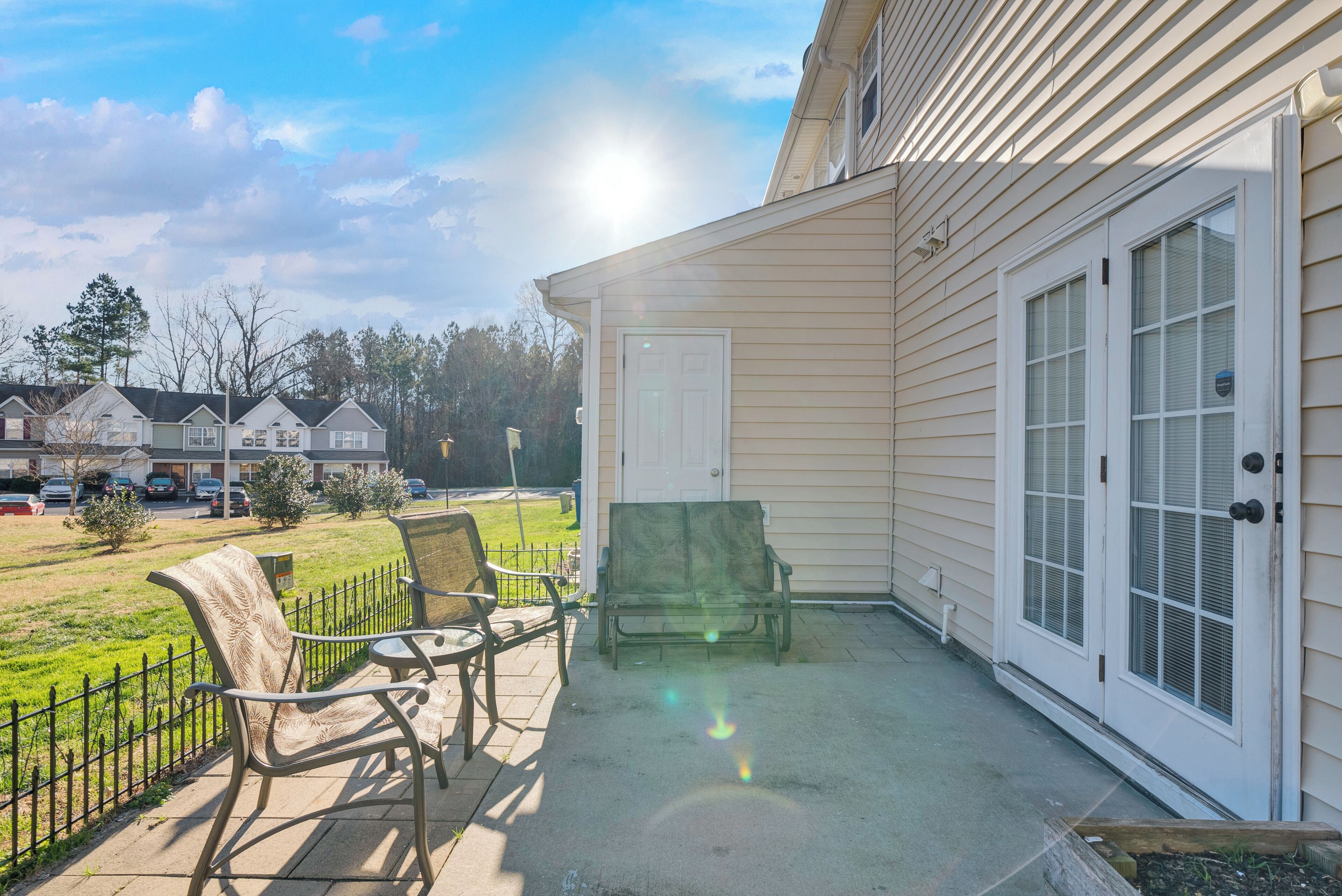 A covered patio area with two chairs and a table, a door, and a view of a residential street.