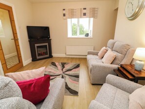 A living room with a fireplace, a sofa set, a television, and a clock on the wall. - BIDDY GRANNY'S, pet friendly in Annagry, County Donegal (County Donegal)