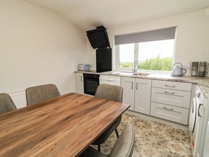 A compact kitchen with a wooden table, white cabinets, a black range hood, and a window with a view of greenery. - BIDDY GRANNY'S, pet friendly in Annagry, County Donegal (County Donegal)