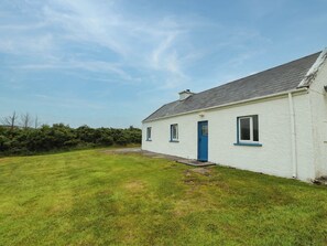 A single-story white house with a blue door and windows, surrounded by a grassy yard. - BIDDY GRANNY'S, pet friendly in Annagry, County Donegal (County Donegal)