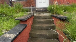 Un edificio de ladrillo con una puerta blanca, número 63, y un pequeño conjunto de escalones de piedra que conducen a la entrada.