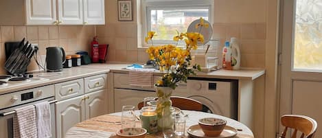 Una cocina con una mesa de comedor para dos, una ventana que ofrece vistas a una casa y una lavadora.