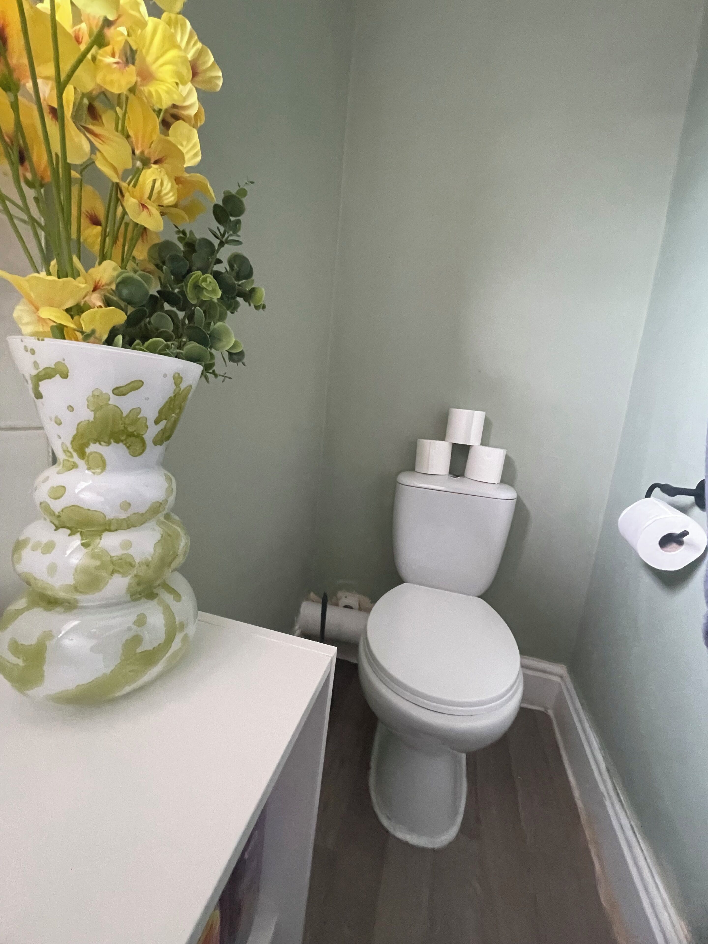 Ein Badezimmer mit Toilette, einem weißen Waschbecken und einer Vase mit gelben Blumen.