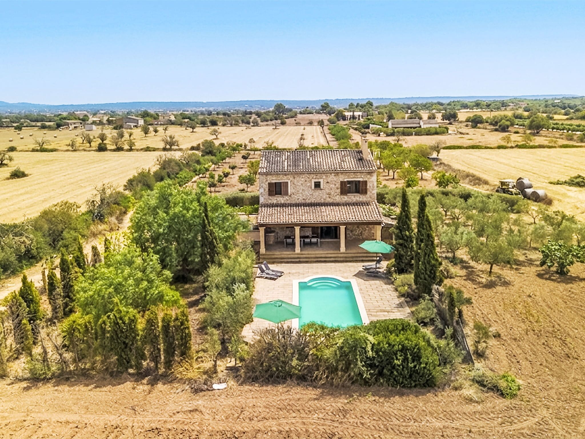 Una casa de dos pisos con piscina, rodeada de campos y árboles.
