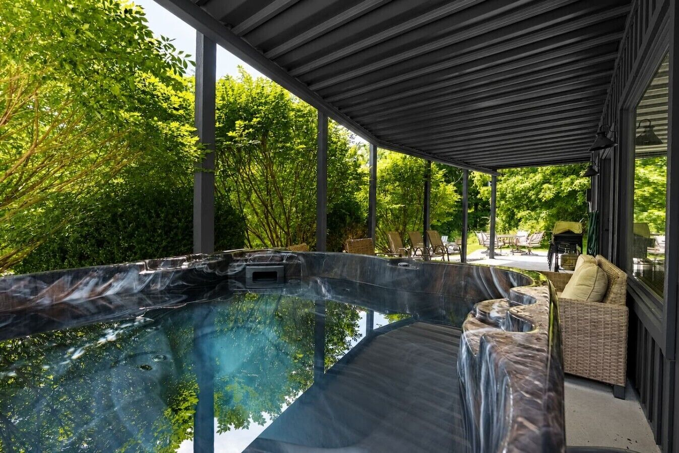 A hot tub area with a covered seating area and a view of lush greenery.