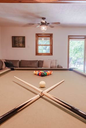 A pool table with a cue ball and billiard balls, a ceiling fan, a window, and a couch in a room. - Houston Lodge: HotTub, GameRoom, Pets, BBQ, Trails (Logan)