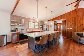 A modern kitchen with a central island, bar stools, wooden flooring, and pendant lighting. - Houston Lodge: HotTub, GameRoom, Pets, BBQ, Trails (Logan)