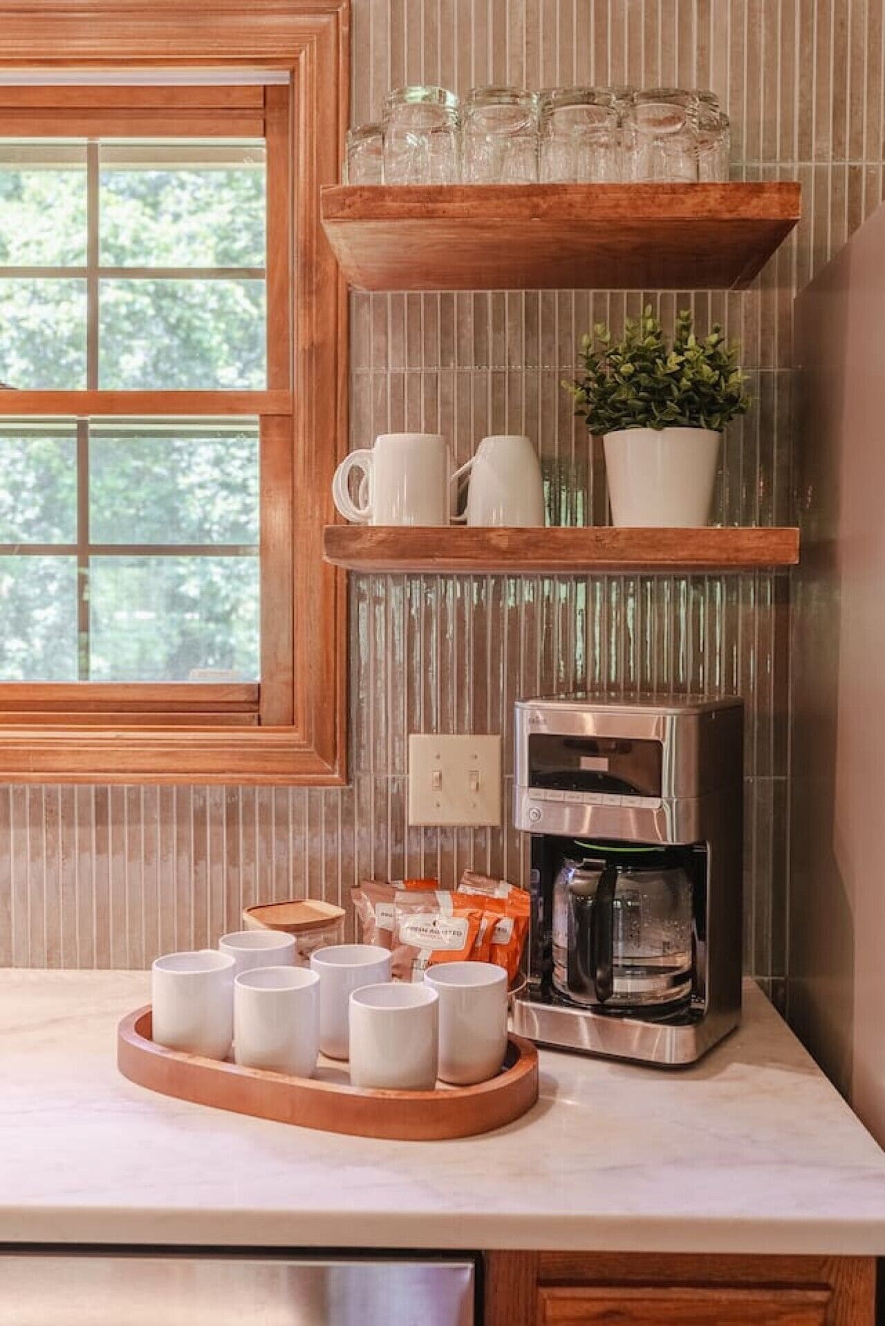 A kitchen with a coffee maker, mugs, and a tray of cups.