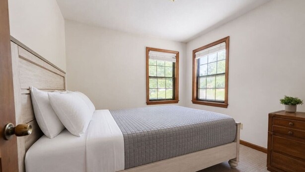Une chambre à coucher avec un lit, deux fenêtres, une commode et une porte.