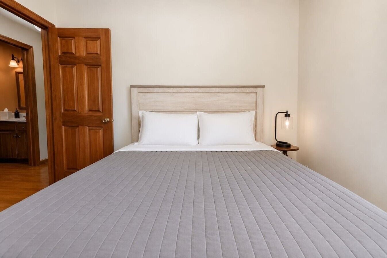 Ein Schlafzimmer mit einem großen Bett, einer Holztür, einem Nachttisch mit Lampe und einem kleinen Schrank.