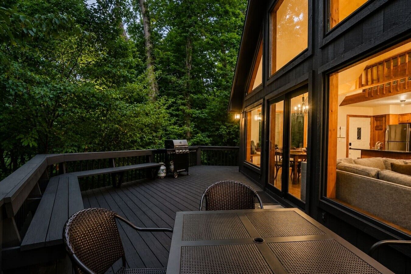 An outdoor deck with a table and chairs, a grill, and a view of the interior.