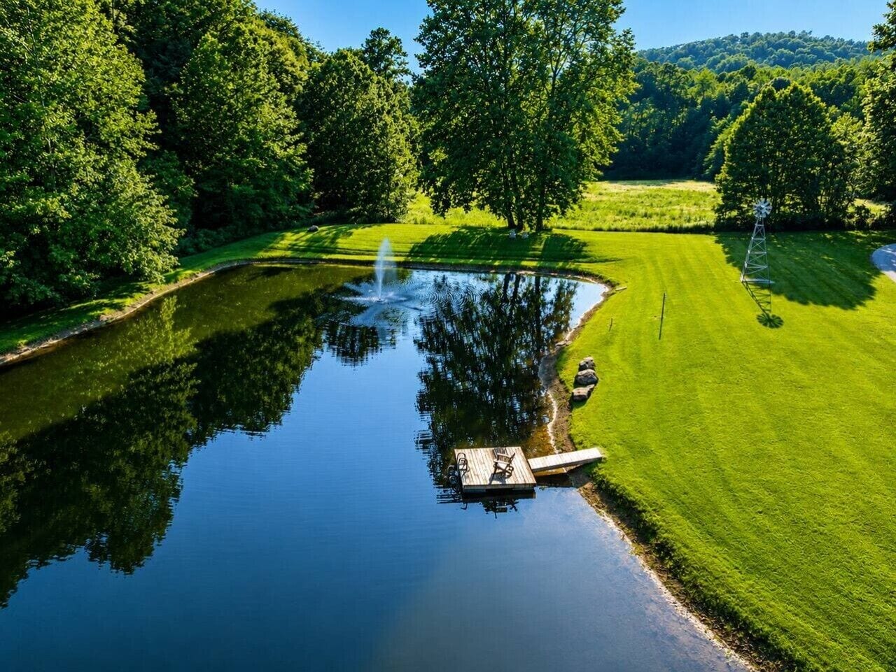 A tranquil pond with a wooden dock, surrounded by lush greenery and a well-maintained lawn.
