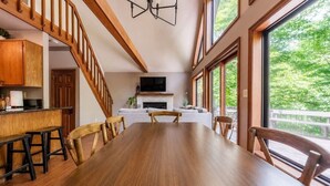 Un vaste espace de salle à manger avec une longue table et des chaises en bois, une cuisine dotée de meubles en bois et une cheminée.