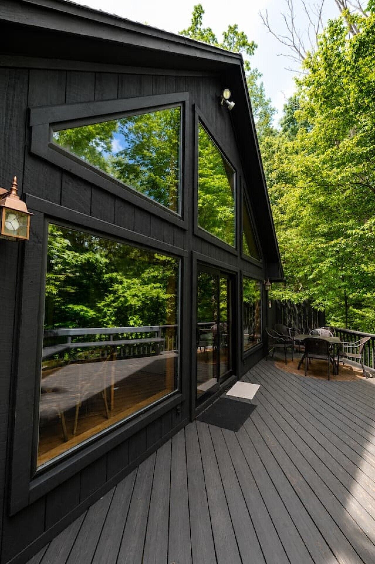 A wooden deck with a railing, large windows, and a view of a forest.