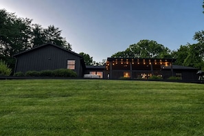 A modern two-story building with a flat roof, large windows, and a covered outdoor area with string lights. - Morehead Lodge | Hot Tub, Game Room, Pet-Friendly (Logan)