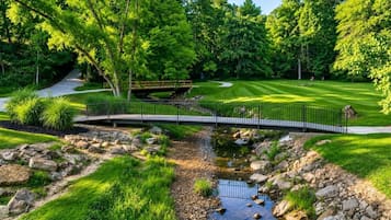 A bridge over a stream in a lush green park with a golf course in the background.
