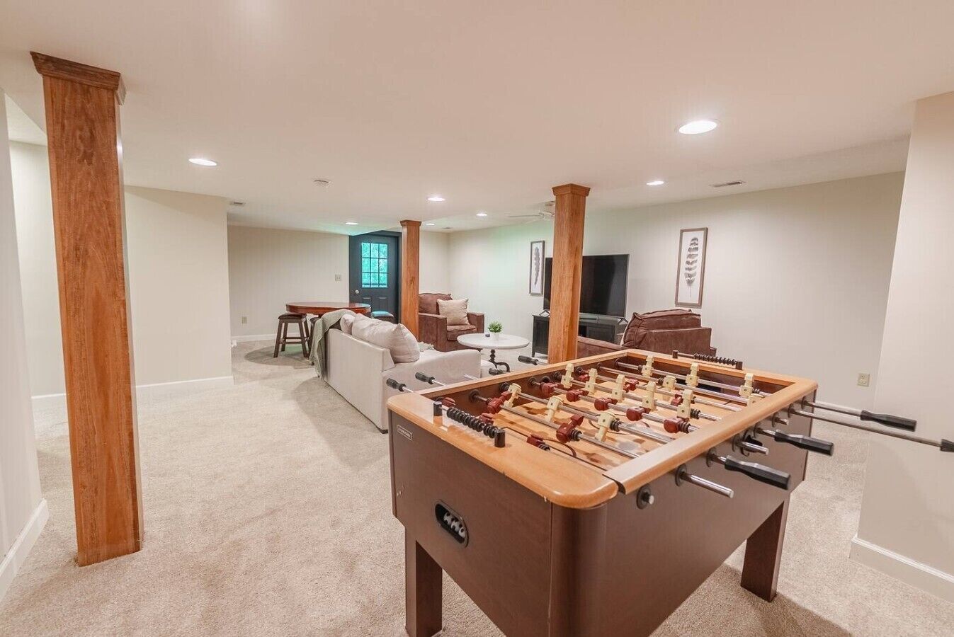 A room with a foosball table, a sofa, a television, and a dining area.