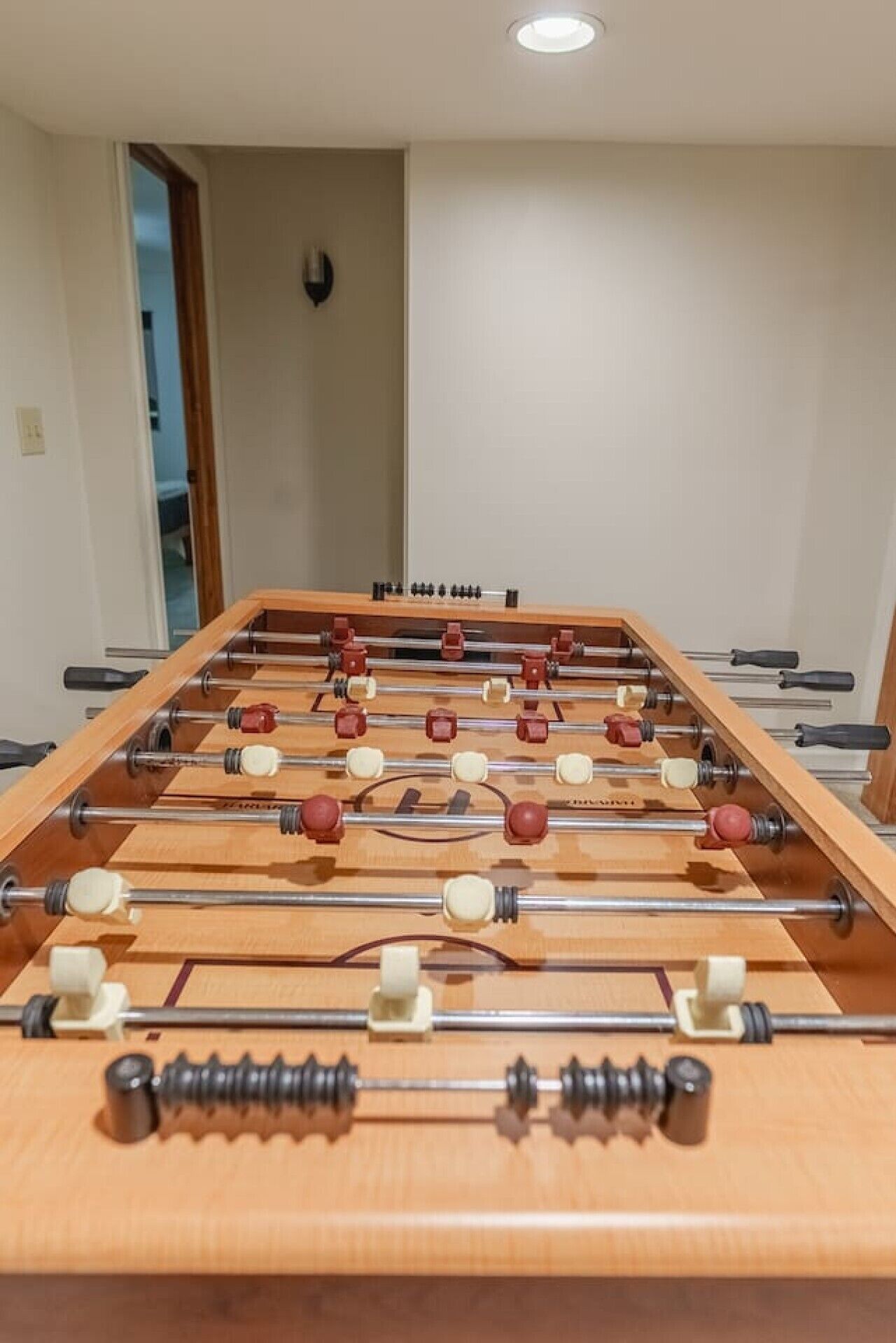 A foosball table in a room with a door and a light fixture on the wall.