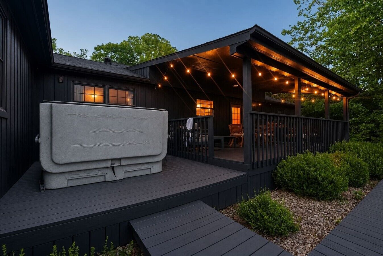A covered outdoor deck with a built-in fireplace, seating area, and string lights.