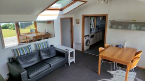 En kompakt bolig med sofa, spisebord, tekøkken og et stort vindue med udsigt til det fri.