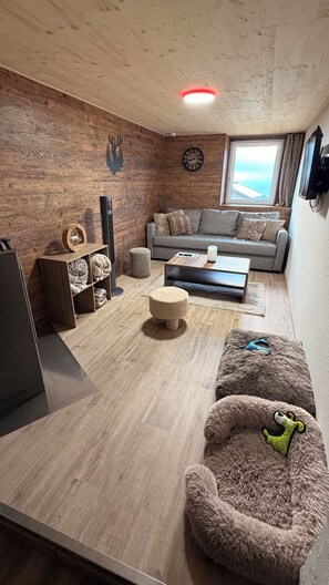 A modern living room with a wooden ceiling, a grey sofa, a coffee table, and a television. - La Bravache - Cozy chalet with an exceptional view (Savièse)