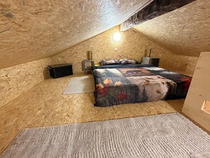 A bedroom with a sloped ceiling, a bed with a patterned bedspread, a bedside table, a lamp, and a rug. - La Bravache - Cozy chalet with an exceptional view (Savièse)