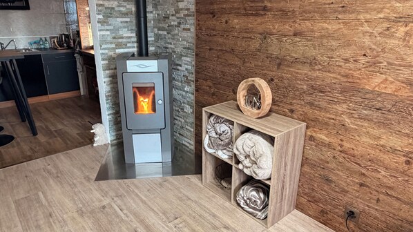 Een moderne keuken met een ingebouwde houtkachel, een houten plank met decoratieve objecten en een achterwand van steen.