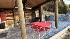 Een overdekt terras met een rode metalen tafel en stoelen, een stenen muur en een open haard van natuursteen.