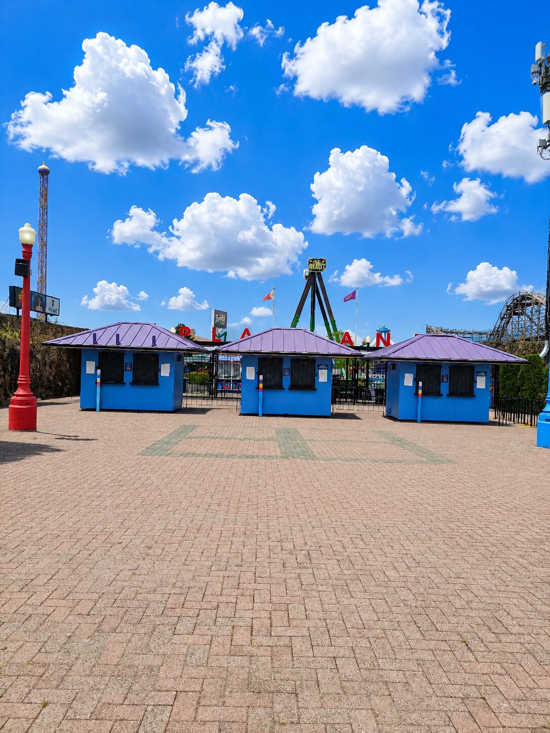 L’entrée d’un parc d’attractions, avec des montagnes russes, des guichets de vente de billets et un ciel bleu dégagé.