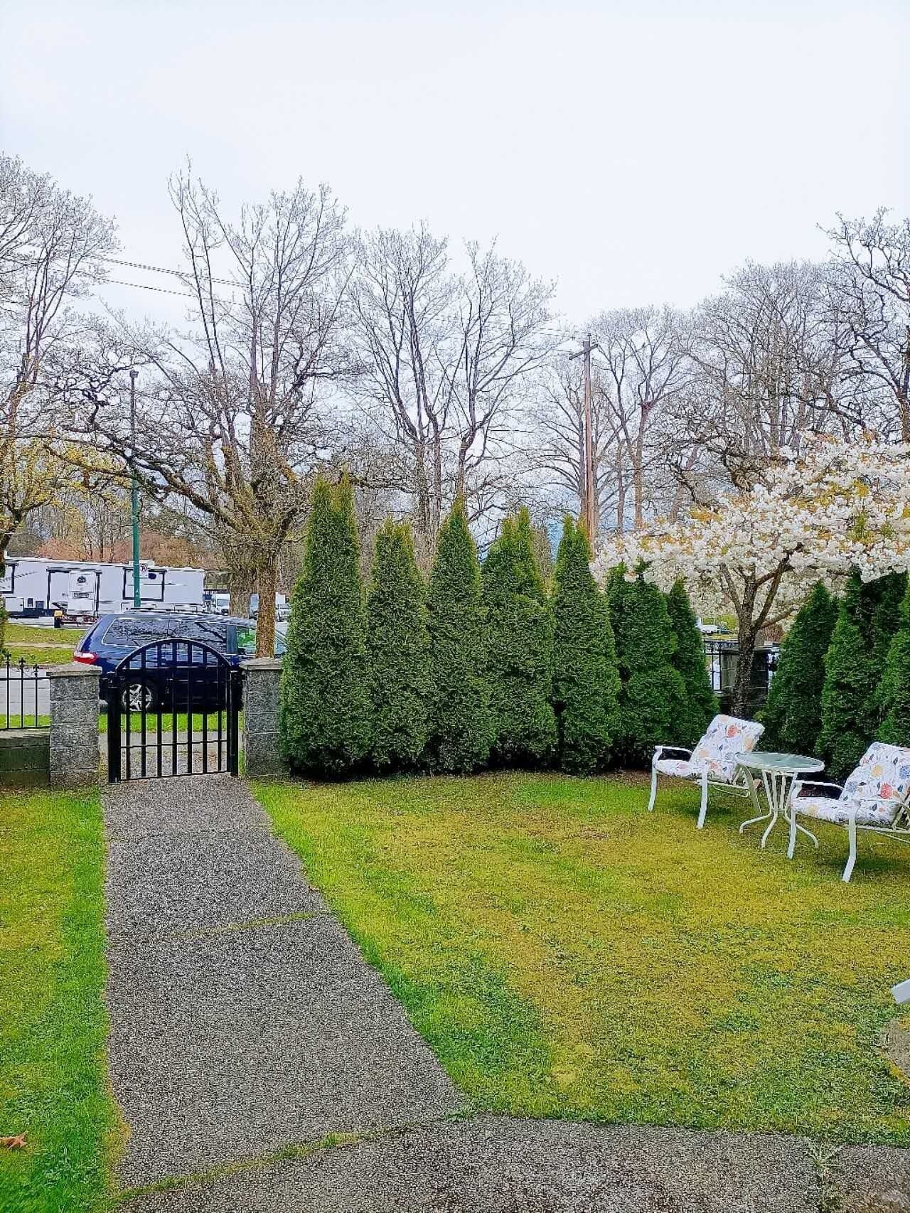 A pathway leading to a gated area with a gazebo, surrounded by neatly trimmed hedges and trees.