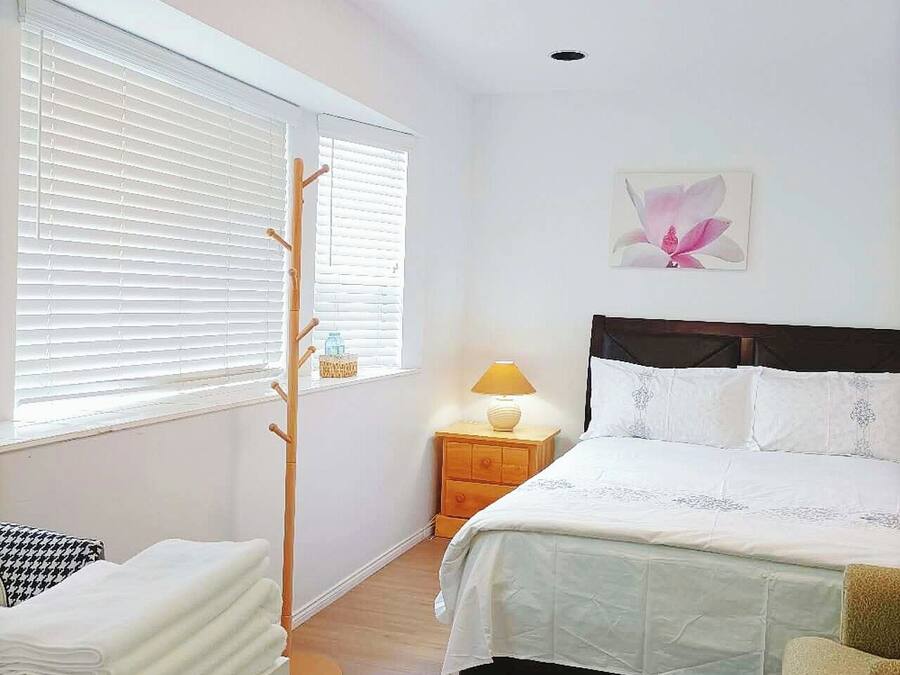 A bedroom with a bed, bedside table, lamp, and a window with blinds.