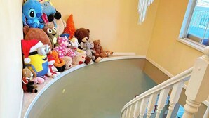 Een houten trap met een witte balustrade die uitkomt op een plateau waar zachte knuffels staan.