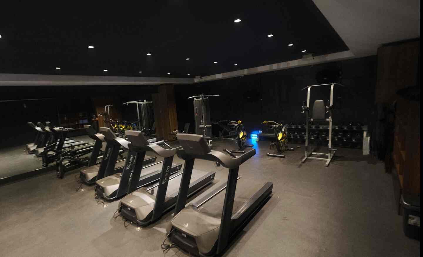 Un gimnasio con cintas de correr, máquinas de pesas y un espejo grande.