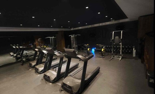 Un gimnasio con cintas de correr, máquinas de pesas y un espejo grande.