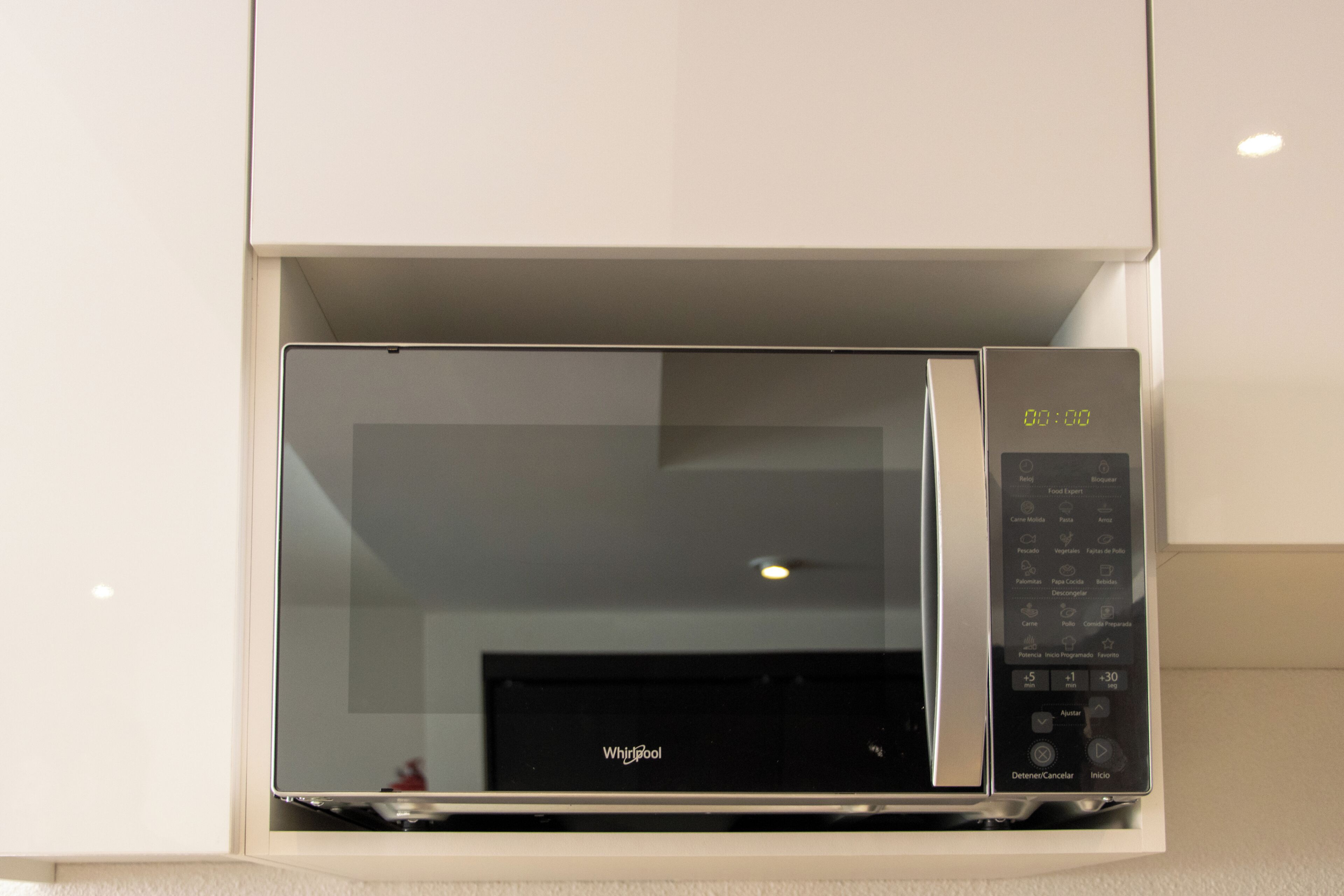 Un horno microondas con pantalla digital y panel de control, integrado en un gabinete blanco.