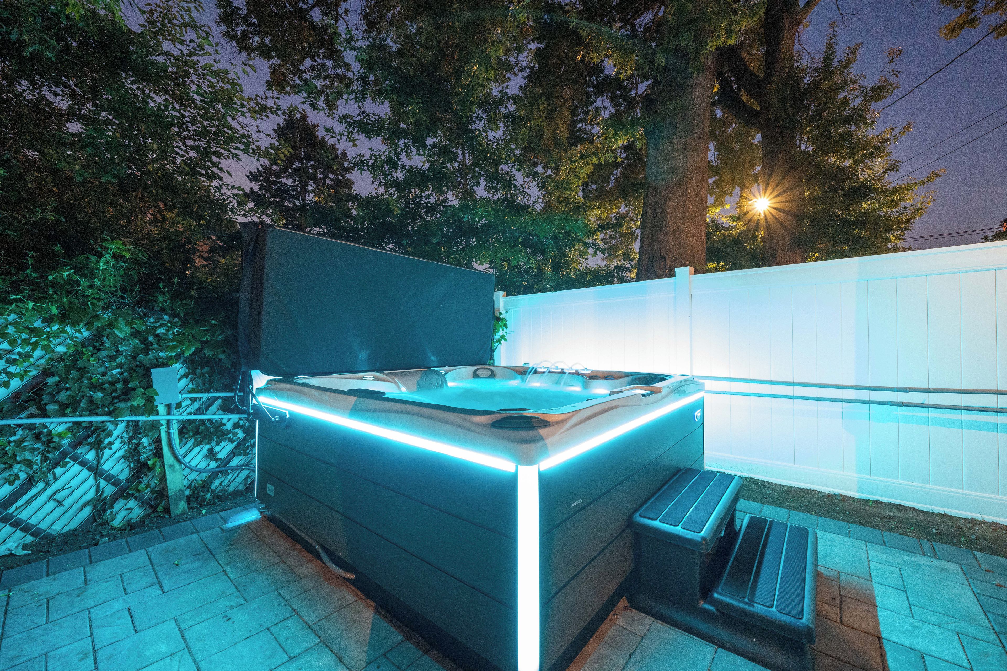 Un jacuzzi exterior con borde elevado y una banca, rodeado por una valla y árboles.