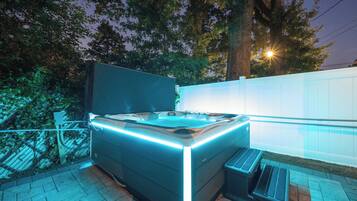 Un jacuzzi exterior con borde elevado y una banca, rodeado por una valla y árboles.