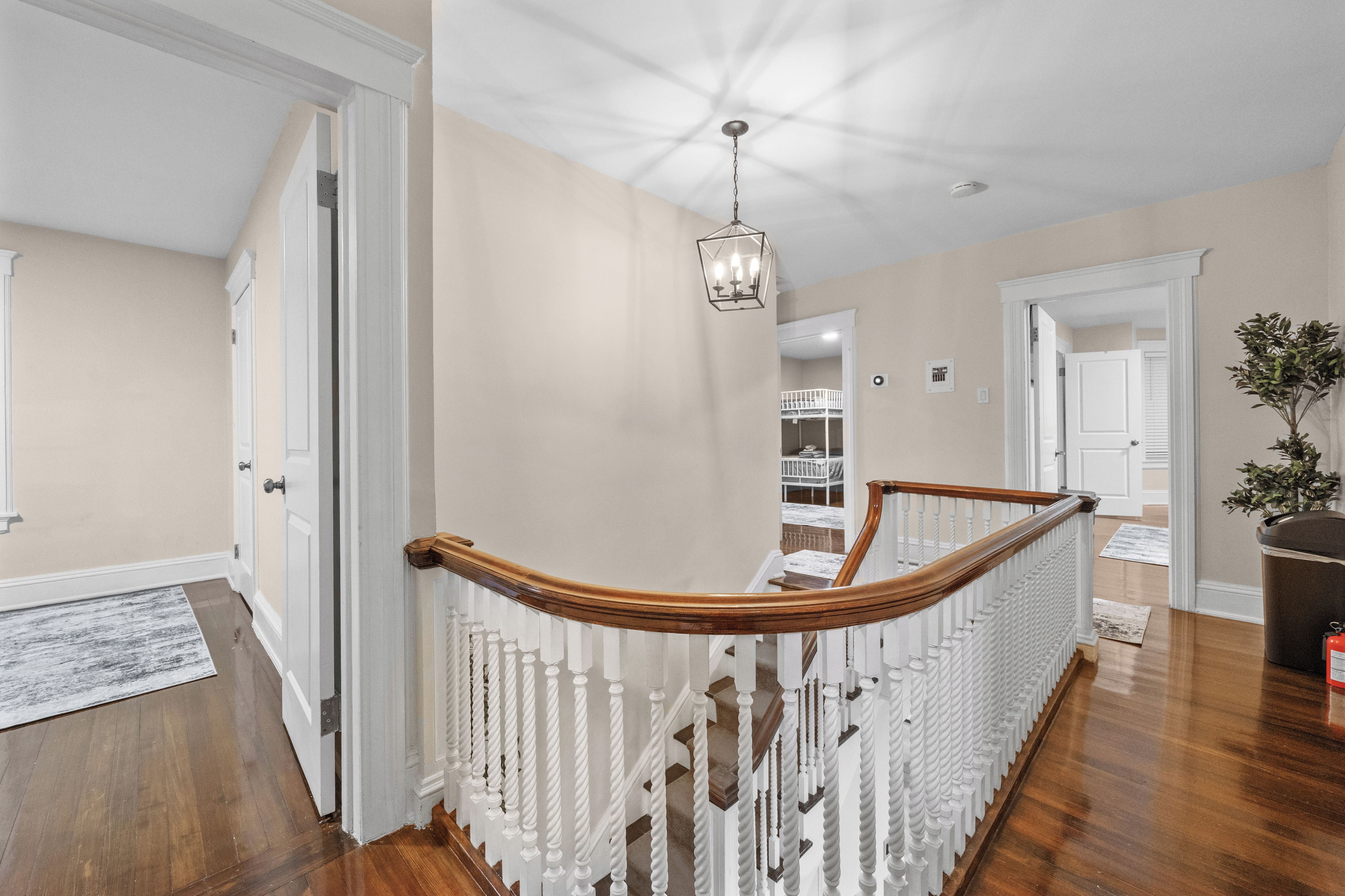 A hallway with a wooden staircase, white railings, and a hanging light fixture.