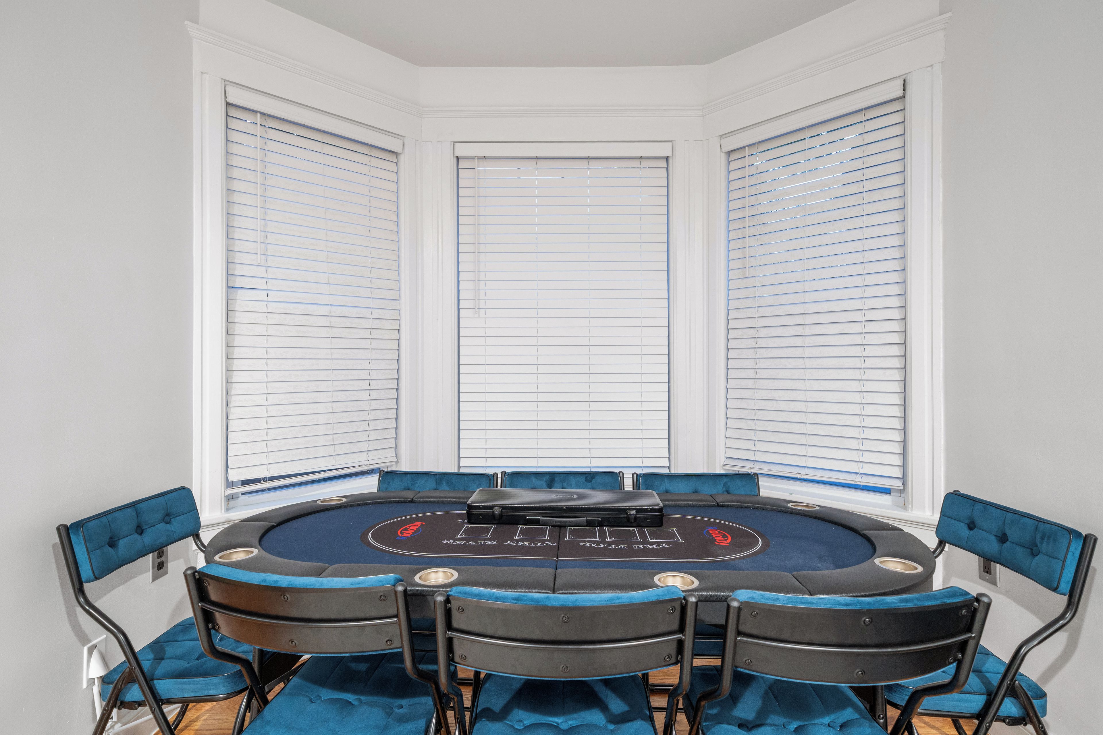 Una habitación con una mesa redonda, sillas tapizadas en azul y una ventana con persianas.
