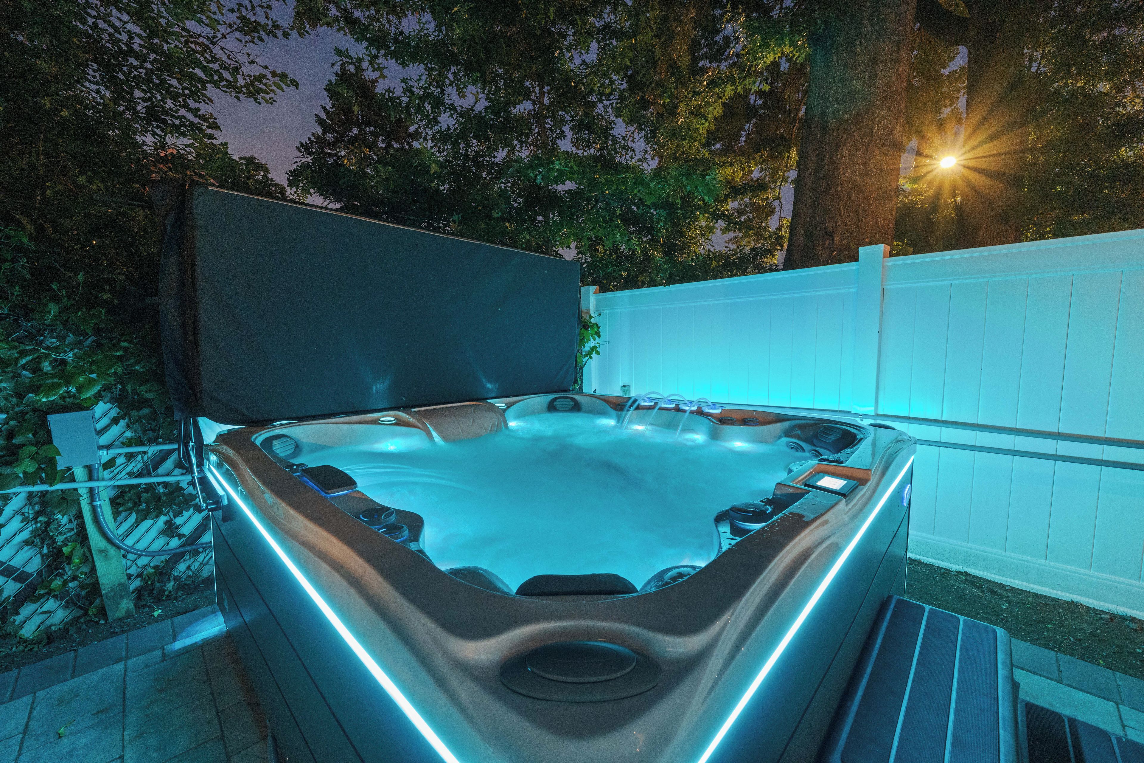 Jacuzzi con borde elevado y asiento integrado, rodeado por una cerca blanca y árboles.