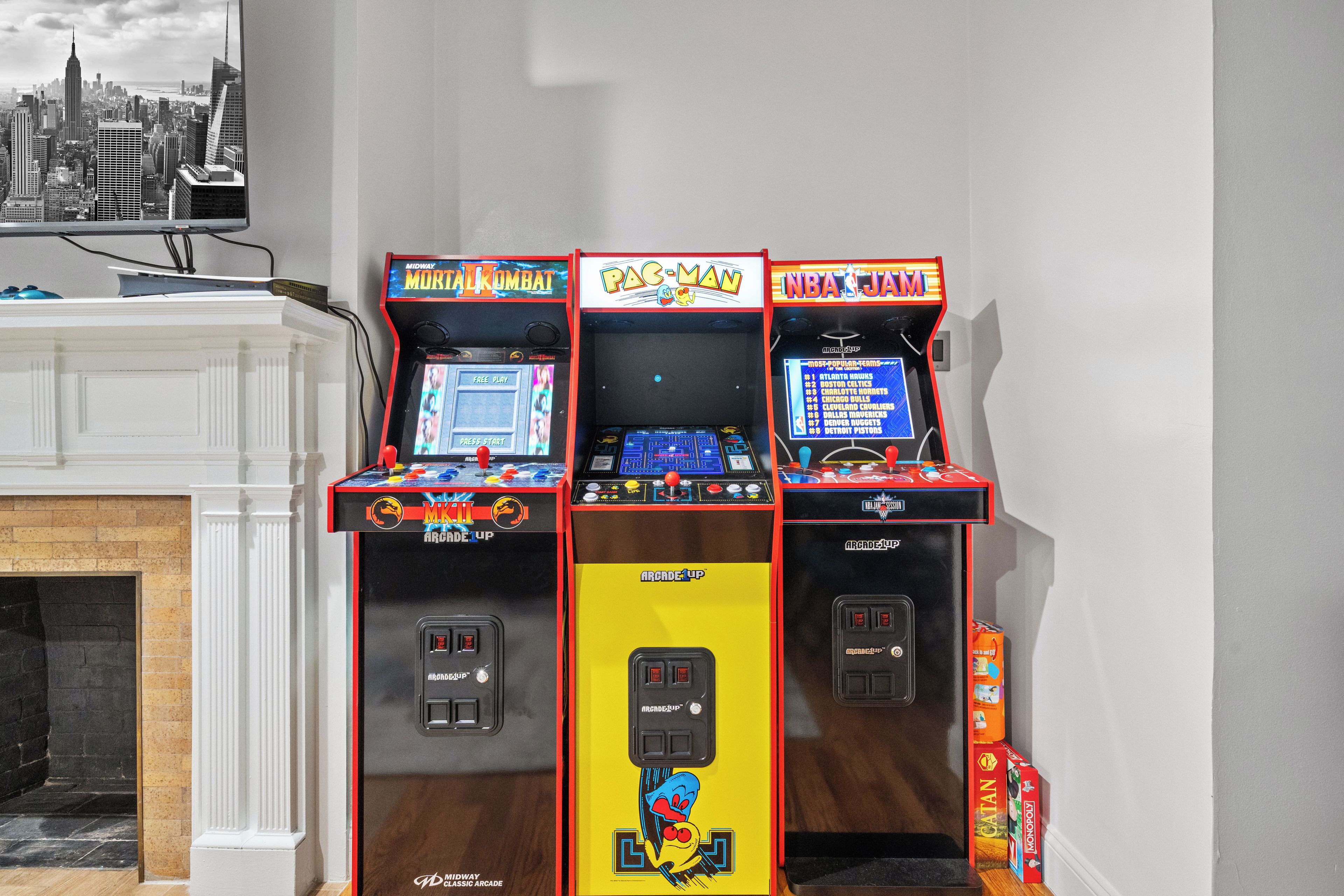 Tres máquinas de arcade, incluyendo Mortal Kombat, Pac-Man y NBA Jam, frente a una pared con vistas a la ciudad.