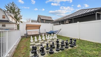 Un patio trasero con un tablero de ajedrez grande sobre el césped, una hamaca y una cerca blanca.