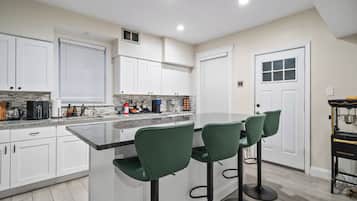 Una cocina con armarios blancos, encimera de granito y taburetes de bar verdes.