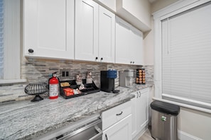 A kitchen with white cabinets, a granite countertop, a coffee maker, and a trash can.