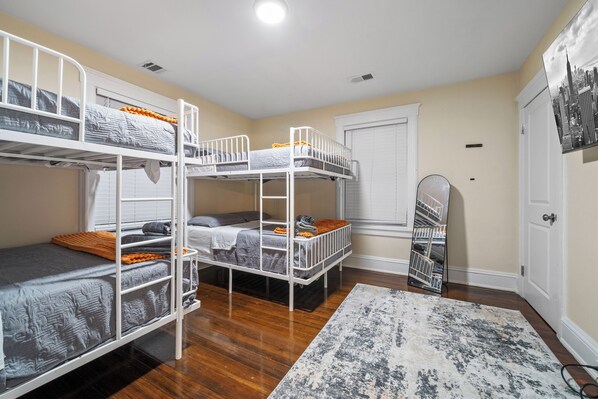A bunk bed room with a wooden floor, a white door, and a cityscape artwork on the wall.