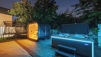 Una sauna al aire libre con un banco y una mesa, rodeada de árboles y una casa.