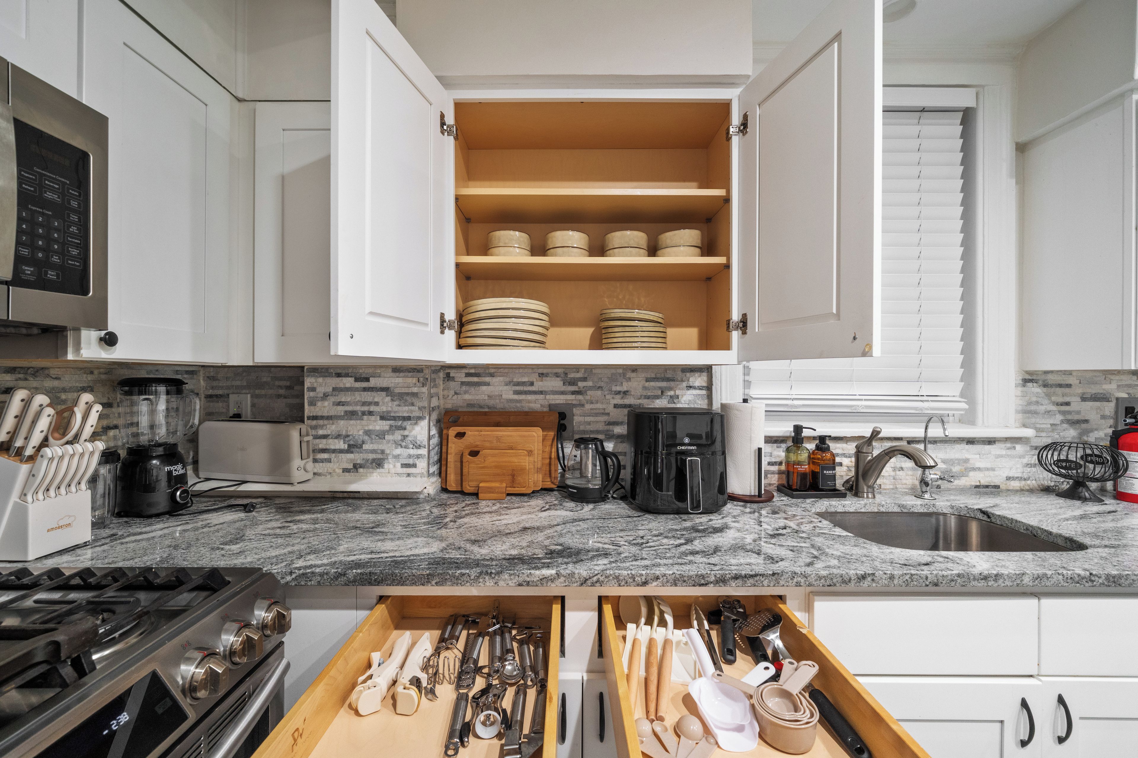 A kitchen with white cabinets, a built-in microwave, a coffee maker, and a drawer with various utensils.